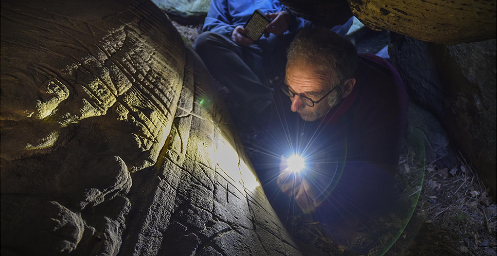 Le chercheur Boris Valentin photographié en train d'observer des gravures préhistoriques dans un abri sous roche 