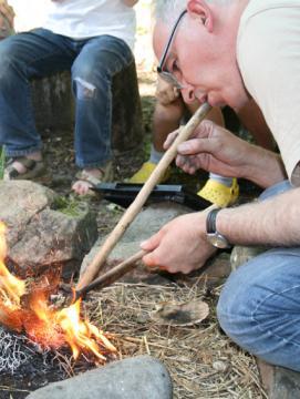 Photographie d'un archéologue attisant un feu en soufflant à l'aide d'un tube creux en bois