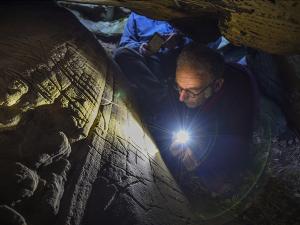 Le chercheur Boris Valentin photographié en train d'observer des gravures préhistoriques dans un abri sous roche 