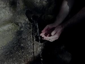 Deux mains jointent récupèrent de l'eau depuis une petit source présente sur un rocher.