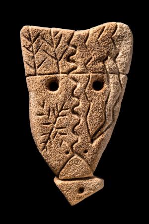 Photographie d'un bloc de grès sculpté en forme de visage et gravé de différents motifs schématiques