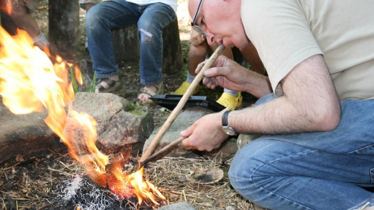 Photographie d'un archéologue attisant un feu en soufflant à l'aide d'un tube creux en bois